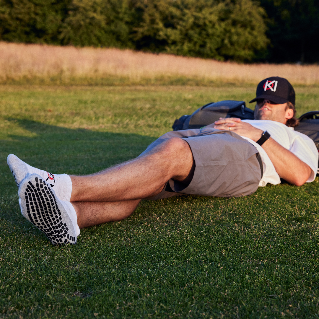 Golfer lying on grass wearing a cap and socks with brand logos