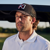 Man wearing a black cap with a logo on a golf course