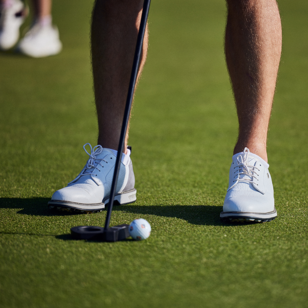 Person preparing to putt on a golf green with white shoes and a golf club.