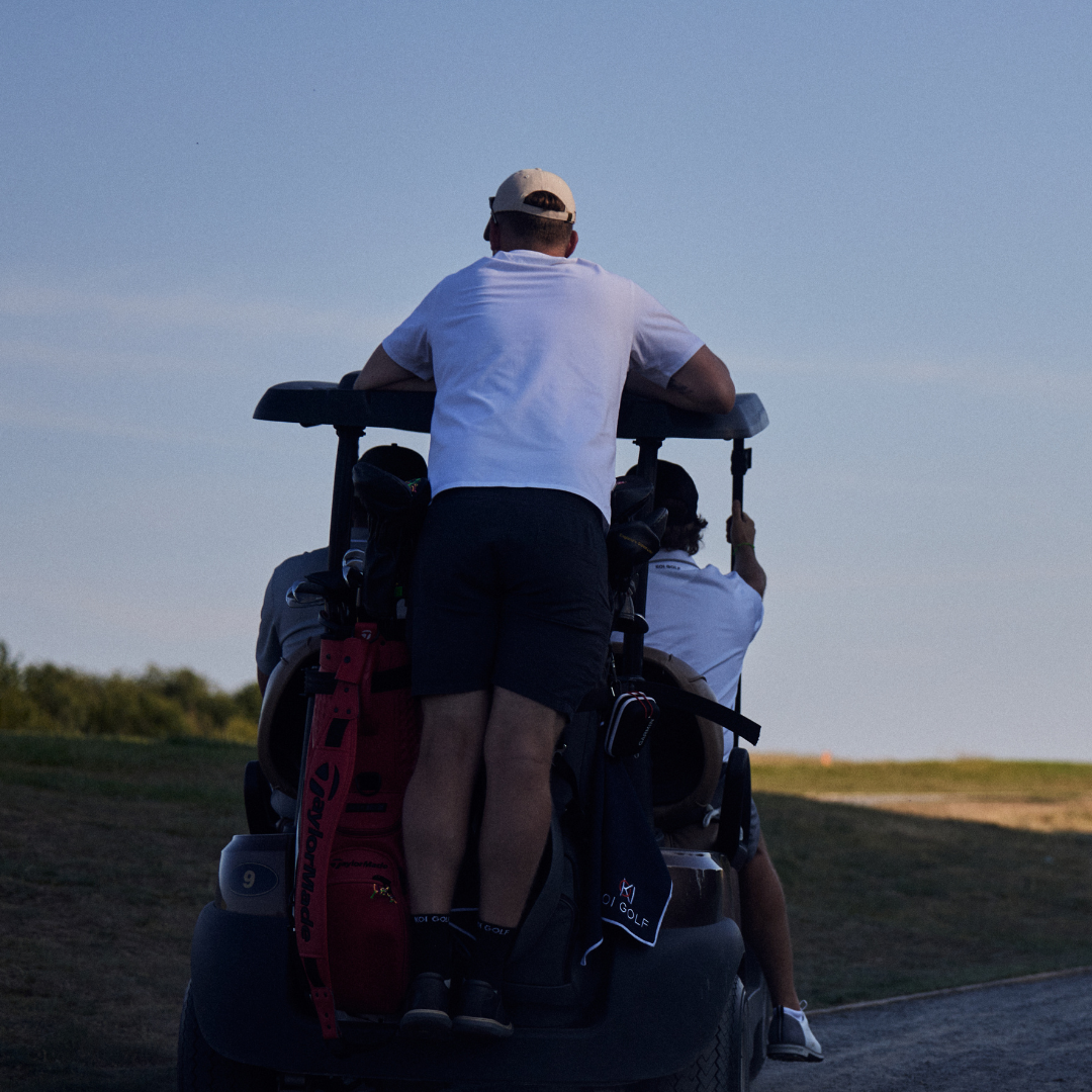 Two people riding in a golf cart on a golf course with a clear sky.