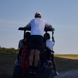 Two people riding in a golf cart on a golf course with a clear sky.