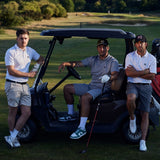 Three men on a golf course with a golf cart, wearing golf polos, one holding a club.
