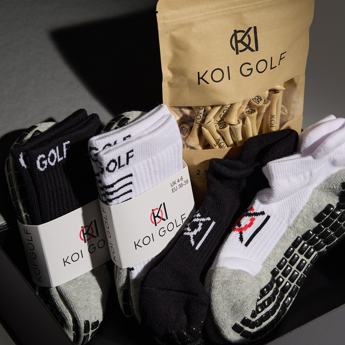 Koi Golf socks and golf tees packaging on a dark surface