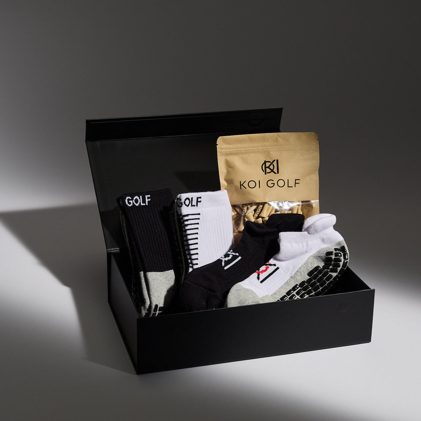 Golf-themed gift set with socks, shoes, and a bag in a black box on a dark background