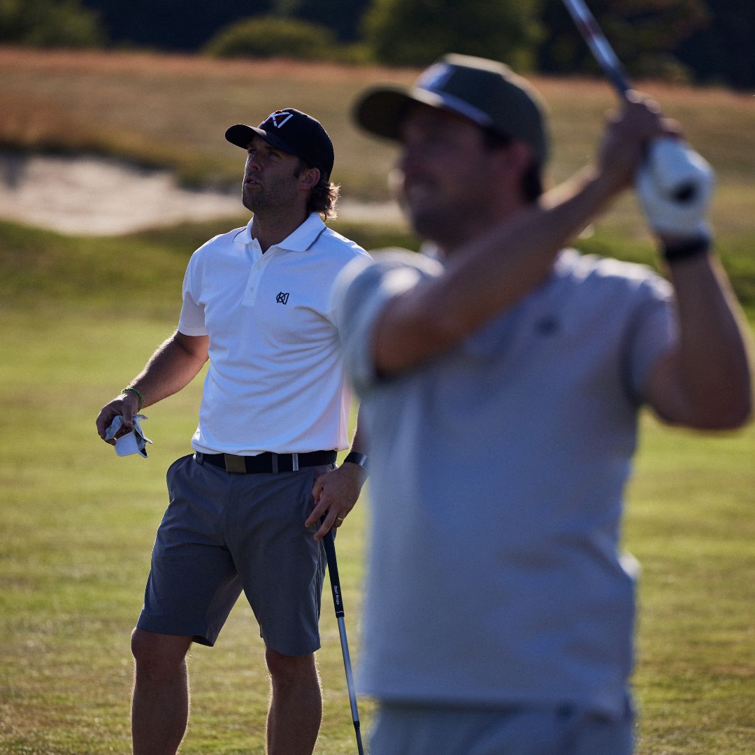 Two men playing golf on a grassy field with one man swinging a golf club.