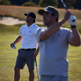 Two men playing golf on a grassy field with one man swinging a golf club.