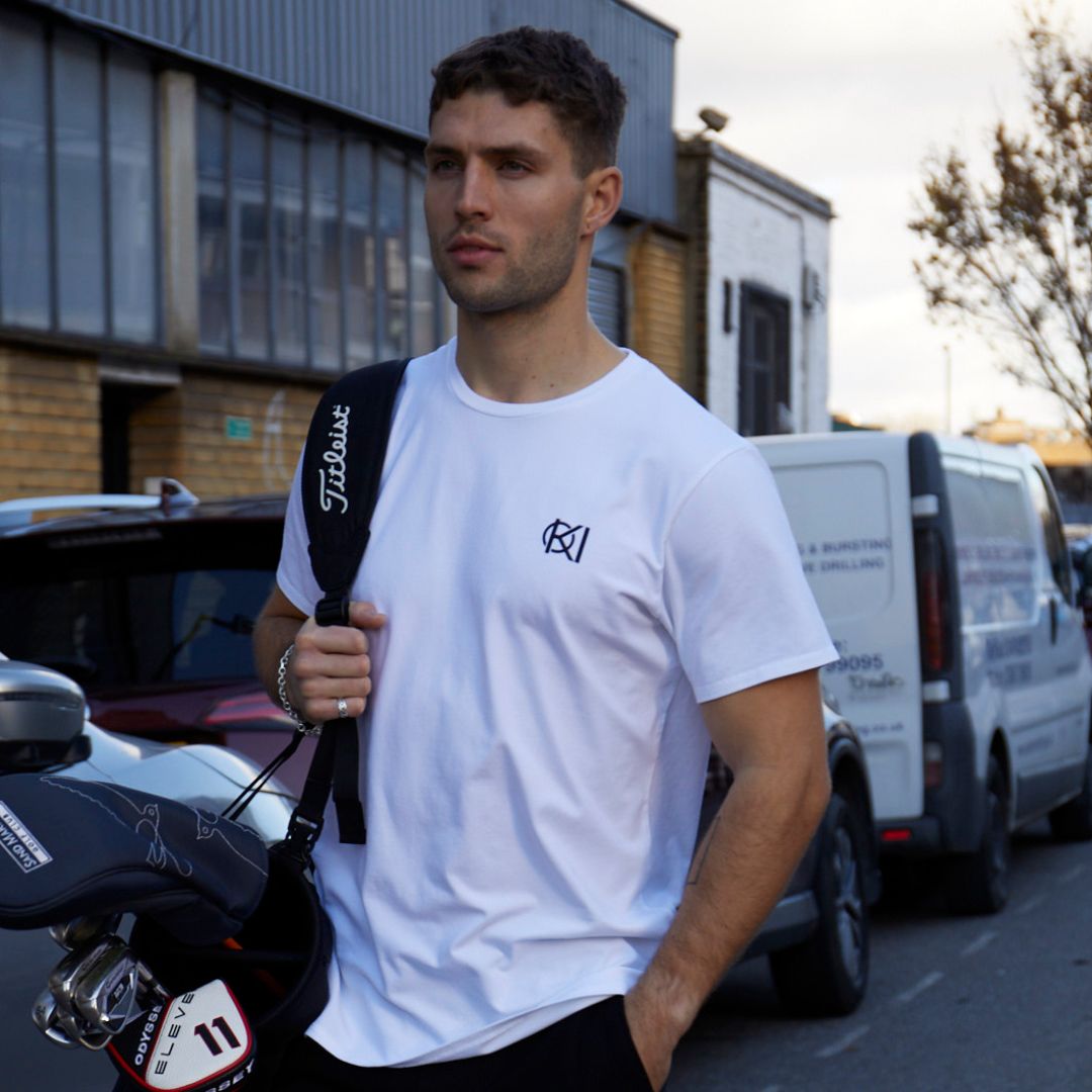 man walks down the street in a white T-shirt with golf clubs.