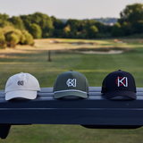 Three caps with different logos on a bench with a golf course in the background