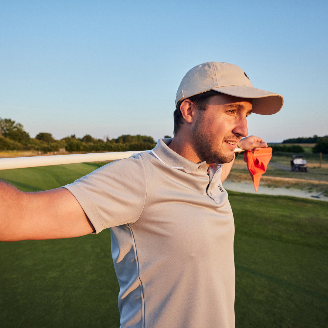 Man on a golf course holding golf flag with cap on