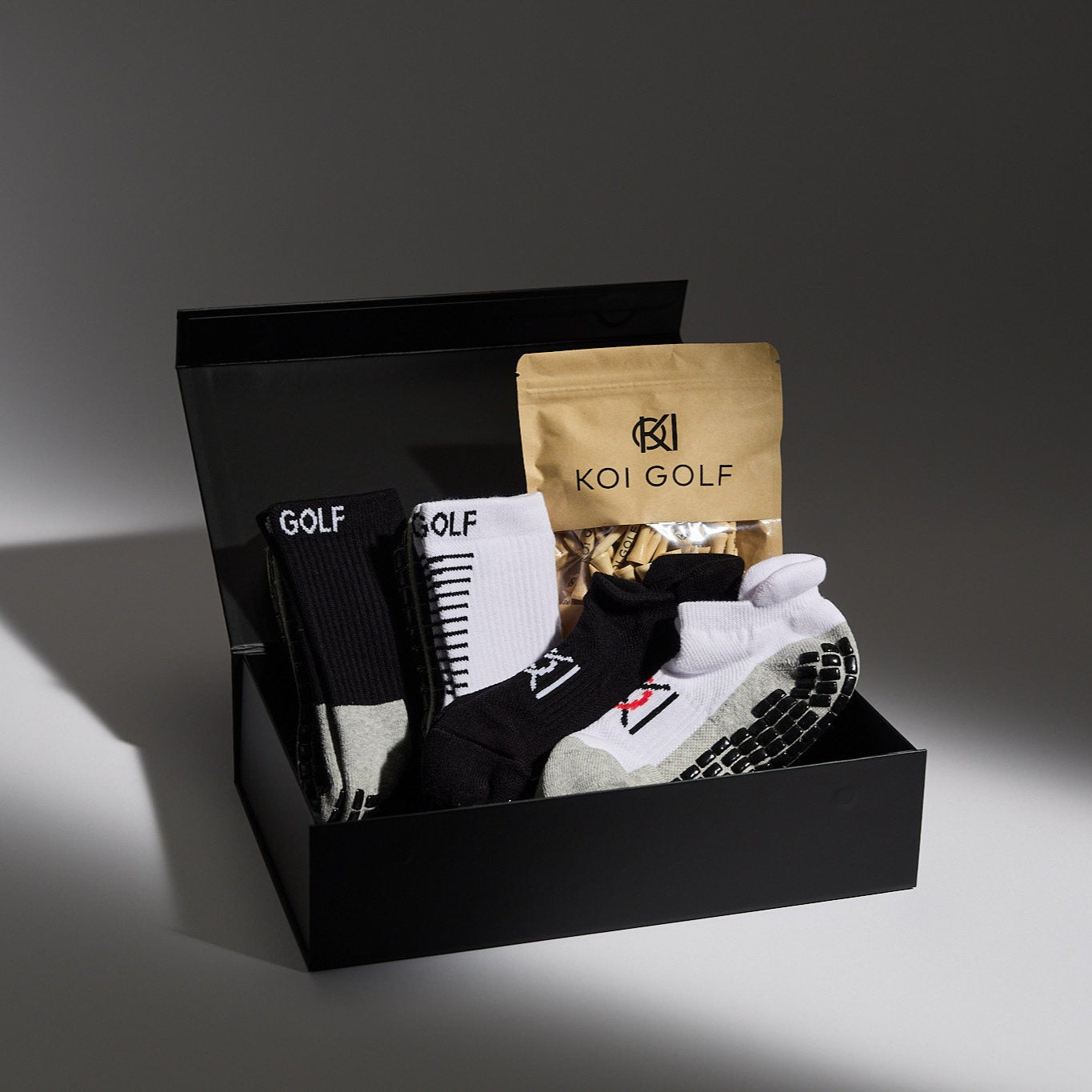 Golf-themed gift set with shoes, socks, and a bag in a black box on a gray background