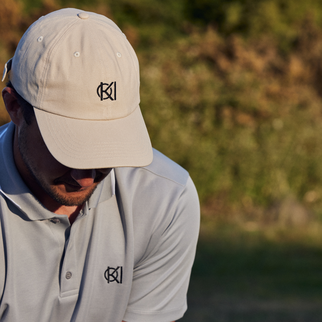 Man wearing a beige cap and light gray polo shirt with a logo, standing outdoors.