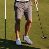 A man on a golf course wearing grey shorts and white socks, holding a golf club.