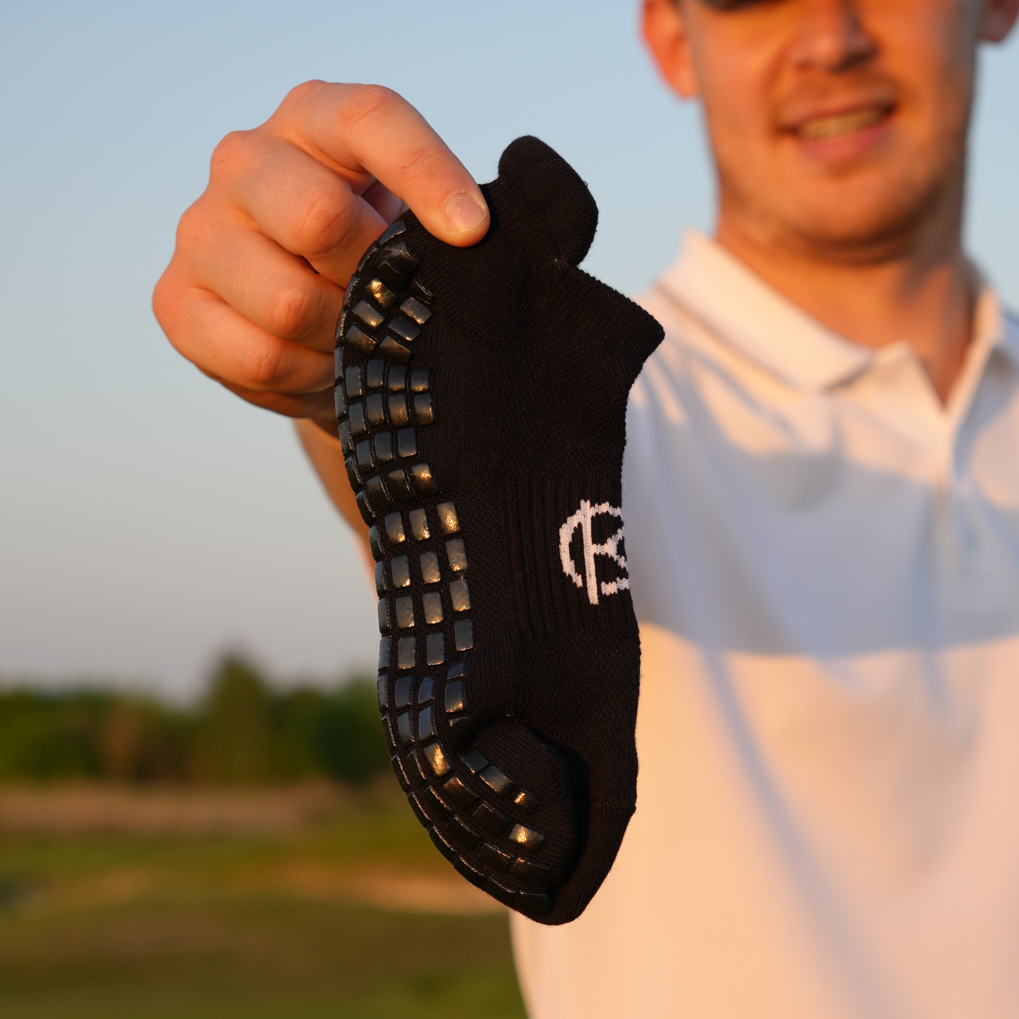 Person holding a black golf sock with a brand logo against a blurred outdoor background.