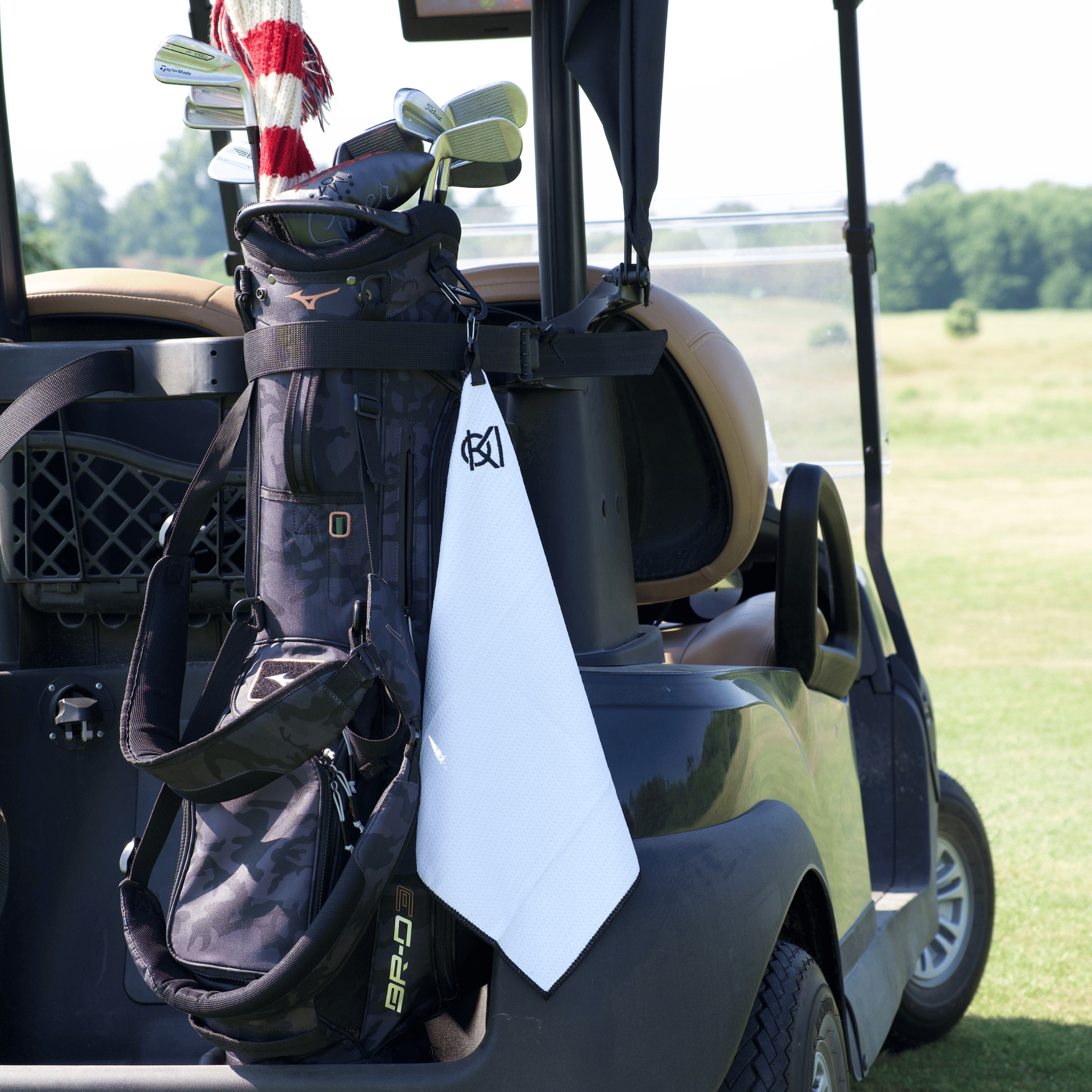 Golf bag with clubs attached to a golf cart on a golf course with a golf towel visible