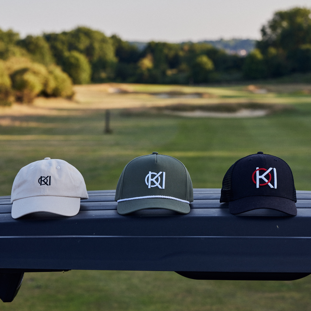 Three caps with different logos on a bench with a golf course in the background