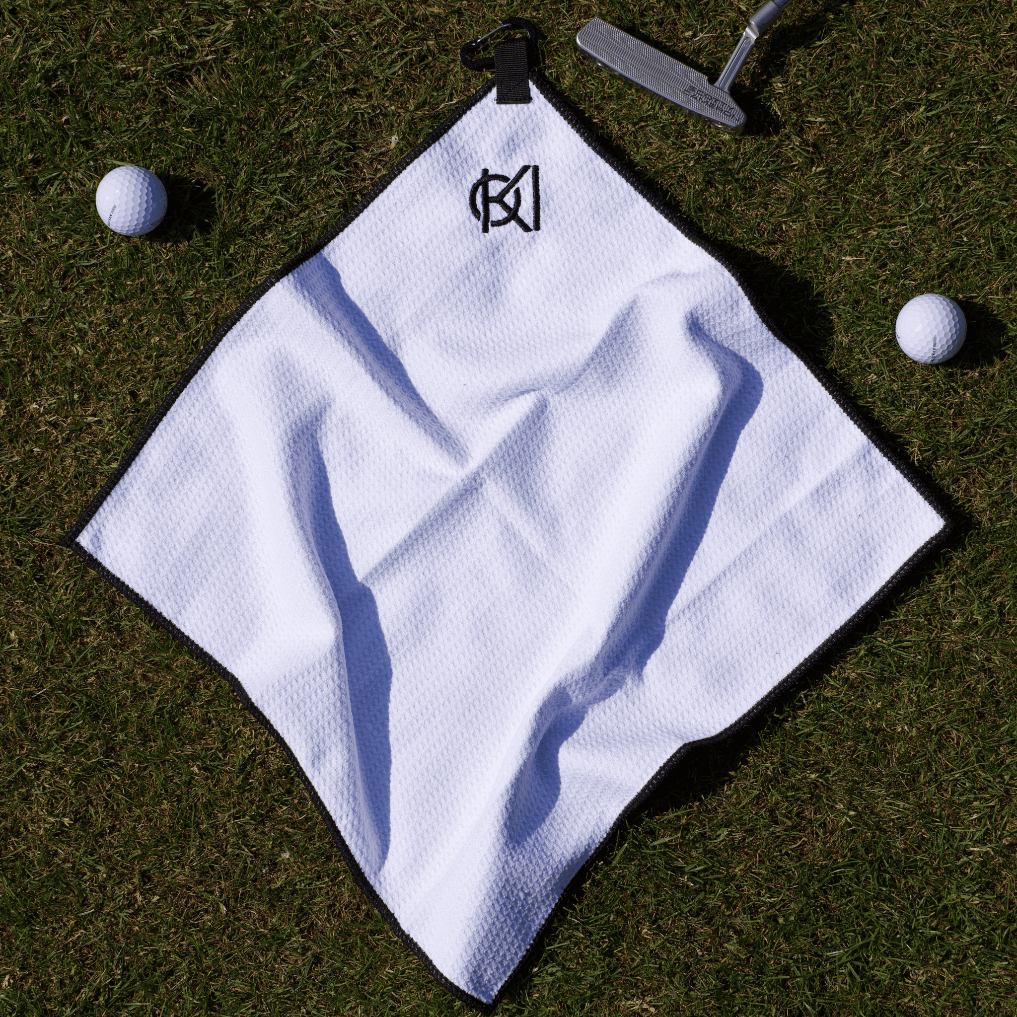 White golf towel with a logo on grass with golf balls and club